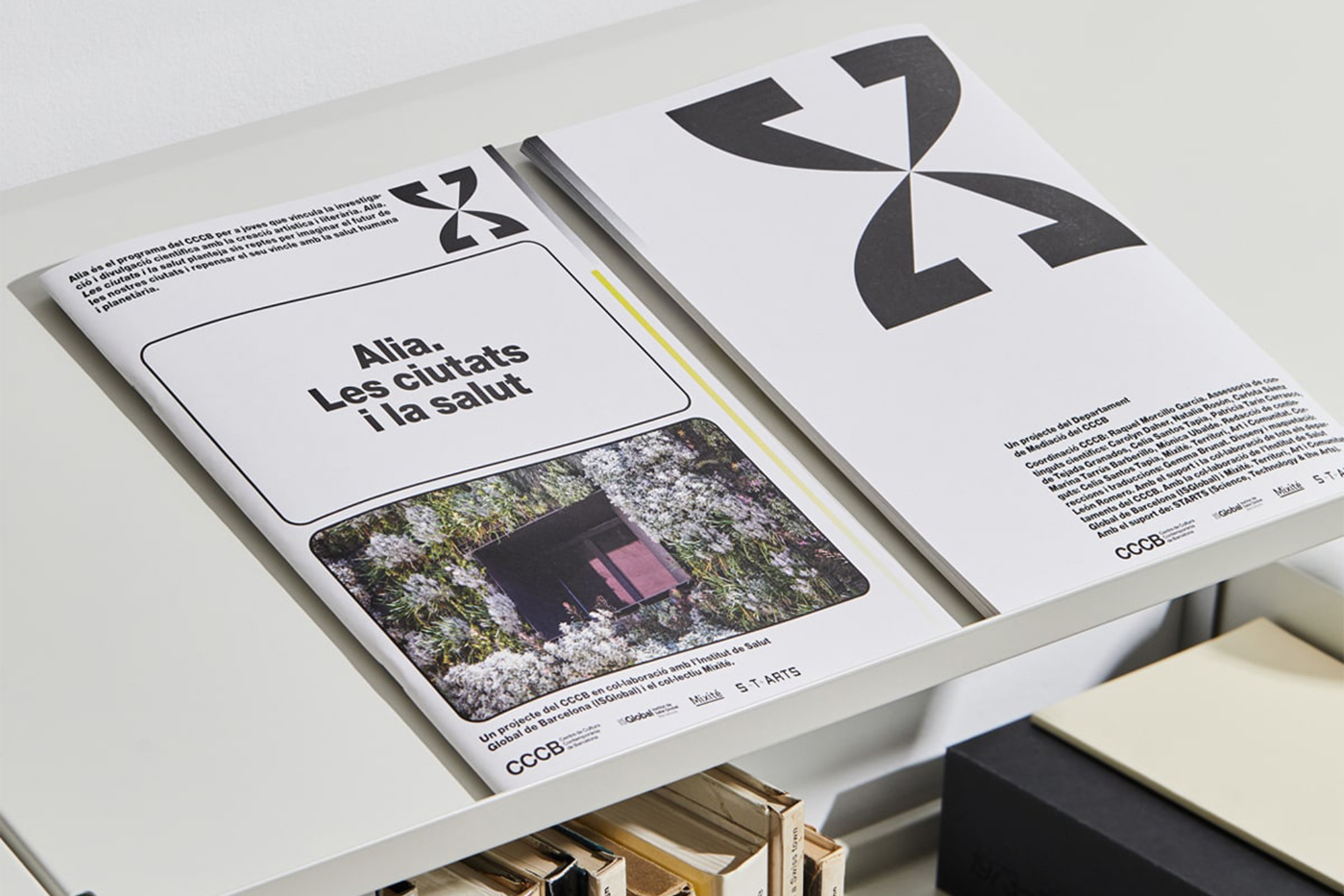 Two magazines are stacked on a white shelf. The magazine covers feature graphic designs and text in black and white.
