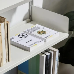 Two white printed booklets resting on a beige metal shelf next to vertical books