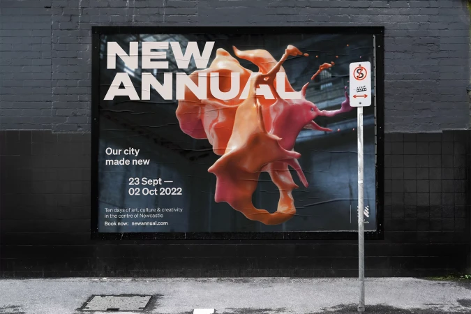 A large outdoor poster mounted on a dark brick wall featuring abstract orange and pink 3D forms and bold typography for New Annual.