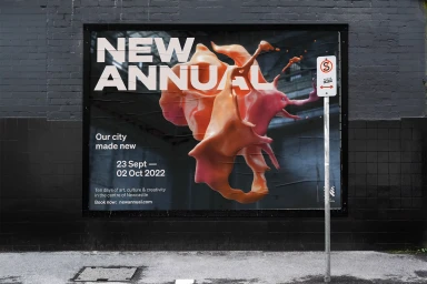 A large outdoor poster mounted on a dark brick wall featuring abstract orange and pink 3D forms and bold typography for New Annual.