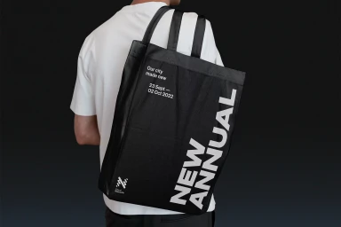 Person wearing a white t-shirt carrying a large black tote bag with bold white New Annual typography on a dark background.