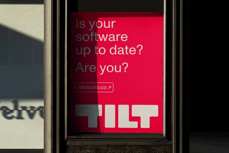A bright pink sign with the brand name TILT in white lettering, asking 'Is your software up to date? Are you?' in direct-eye-level outdoor shot.