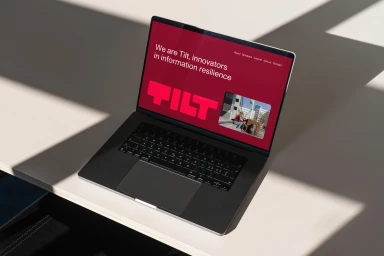 Laptop computer on a pale desk displaying the TILT brand website with a red homepage UI.