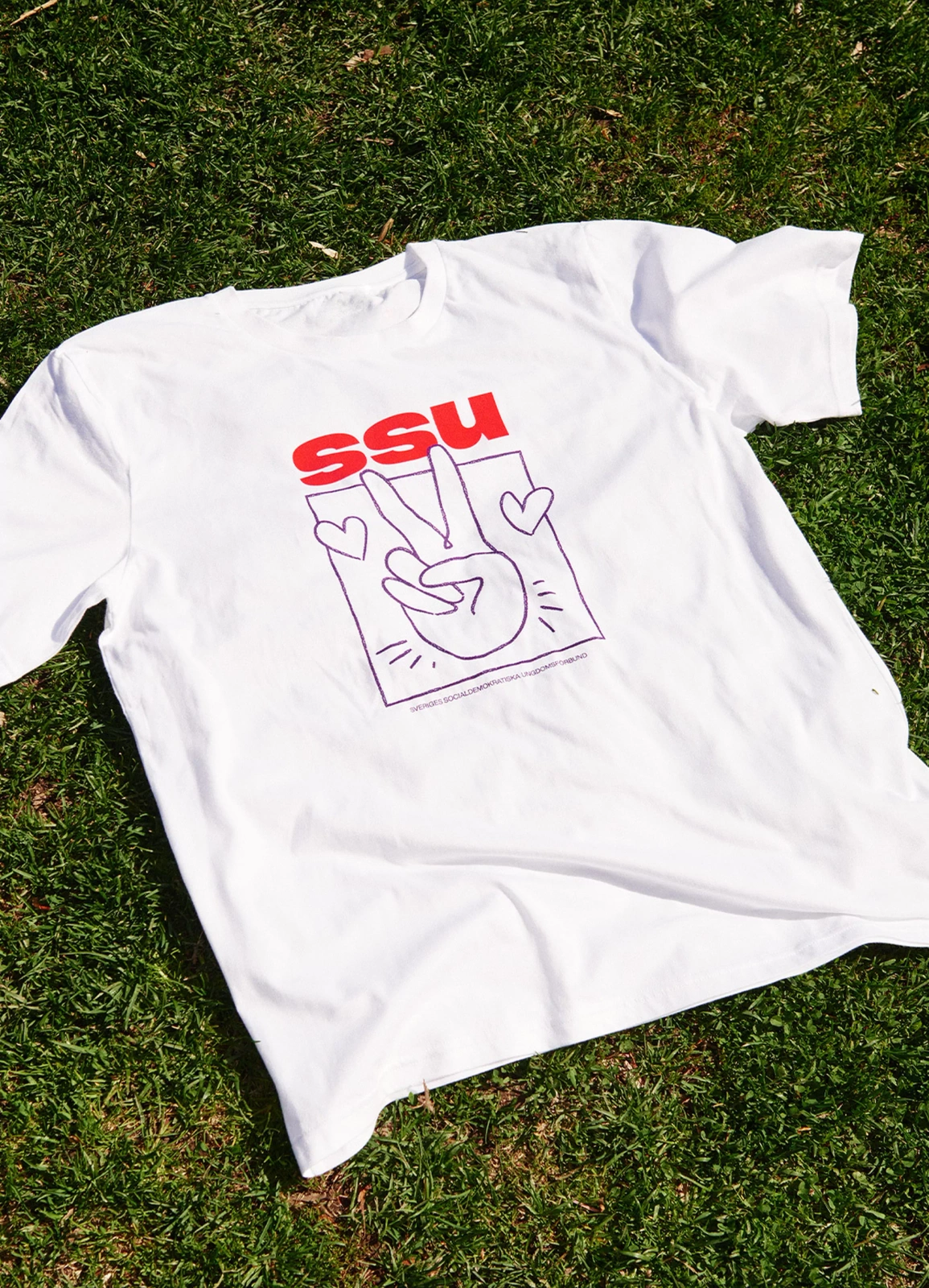 White t-shirt with red and purple SSU graphic print laid flat on green grass.