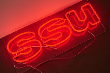 Bright red neon sign displaying the letters SSU mounted on a clear acrylic backing against a dark background