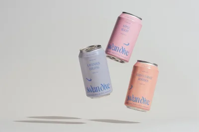 Three floating beverage cans in pastel pink and lavender shades against a light grey studio background.