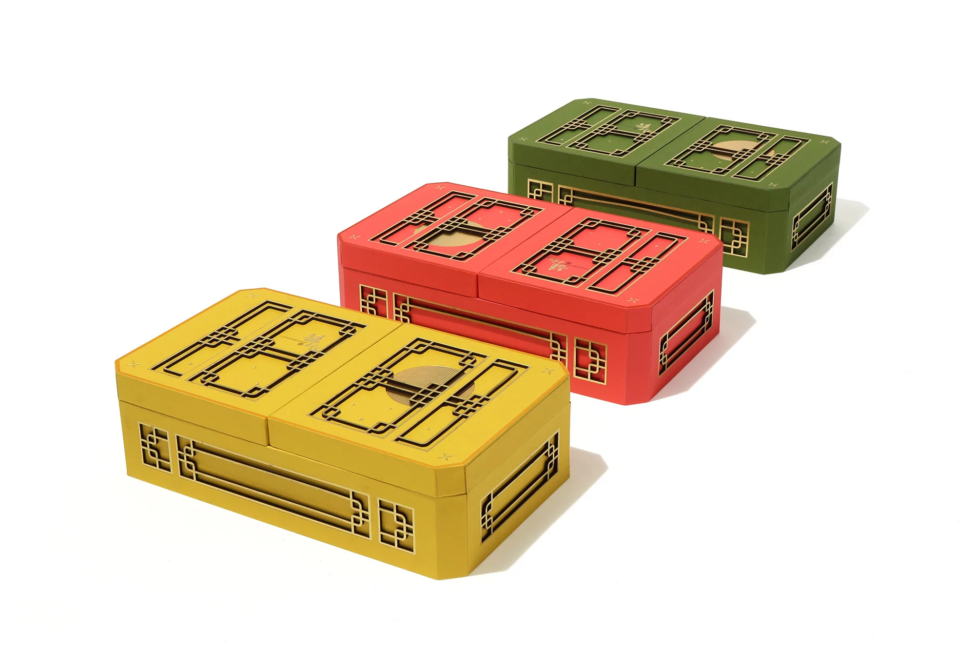 Three colorful, decorative boxes with geometric designs in yellow, red, and green, arranged on a clean white background, shot in studio.