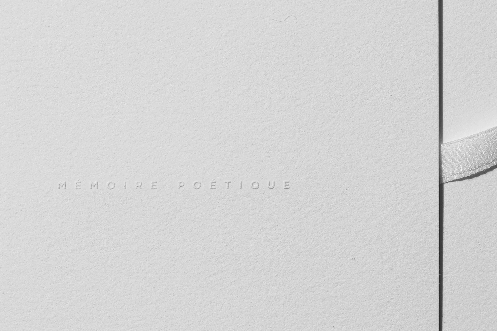 Elegant embossed 'Memoire Poetique' on textured white card stock, secured with a satin ribbon. Minimalist aesthetic with focus on texture.