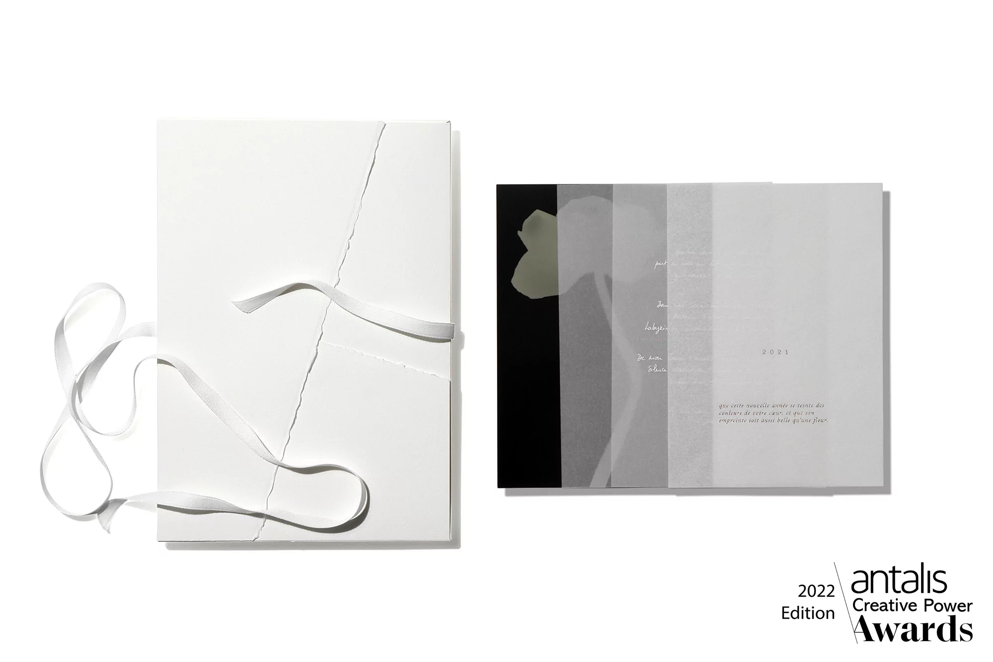 Two white hardcover books, one tied with a white ribbon, are displayed on a white surface in a bright, minimalist composition.