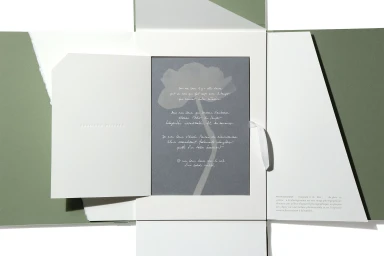 Open sage green paper packaging folder revealing a white card insert and a dark grey card with white handwritten text.