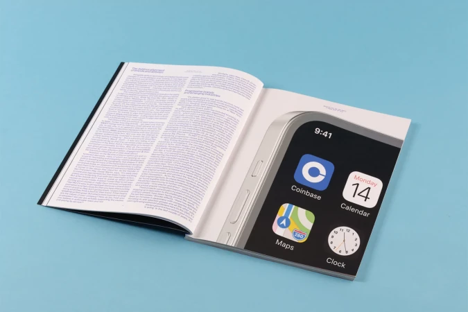 Open book displaying a digitally enhanced smartphone mockup, featuring the Coinbase and Maps app icons against a light blue backdrop.