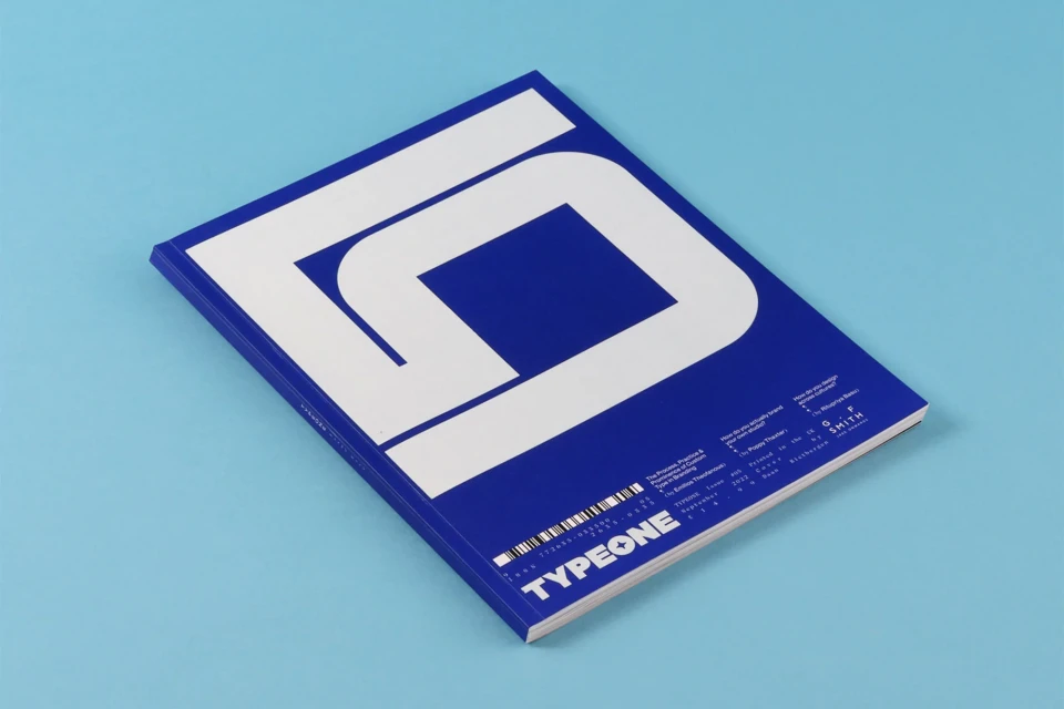 A dark blue TYPEONE magazine with bold white lettering lies diagonally against a light blue background, showcasing modern design.