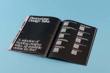 An open magazine layout featuring bold white typography and QR codes on black pages against a solid blue background.