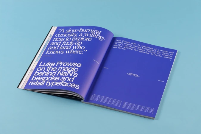 An open magazine spread featuring bold white typography on vibrant blue pages against a solid blue background.