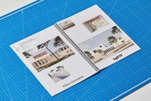 A spiral-bound presentation booklet featuring architectural imagery laid open on a blue grid cutting mat.