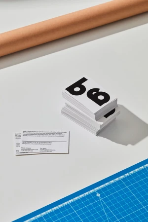 Stack of business cards with bold typography resting on a white surface alongside a blue cutting mat and craft paper roll.