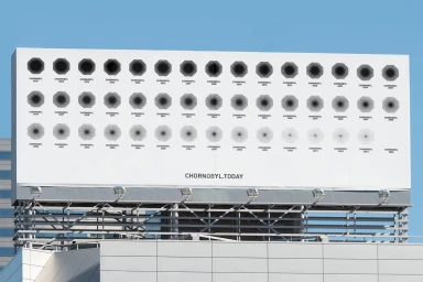 Large outdoor billboard displaying a white background with a grid of black radial graphic symbols and website text against a blue sky.