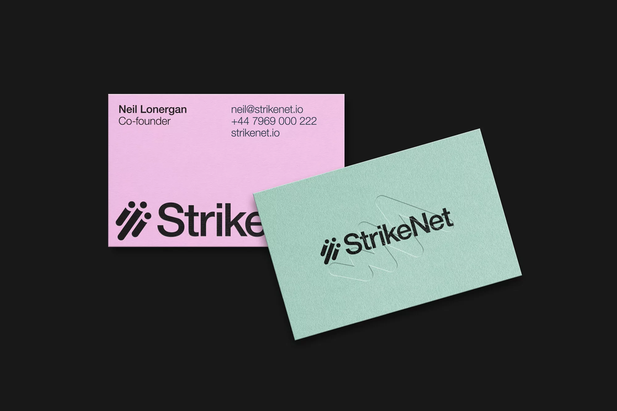 Two business cards with the StrikeNet logo, one pink and one green, are angled on a black surface with contact information.