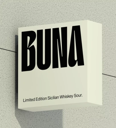 Black BUNA text on a square ivory sign attached to a speckled grey wall, promoting a Limited Edition Sicilian Whiskey Sour.