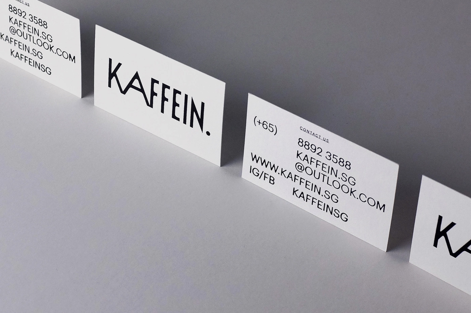 Minimalist business cards arranged in a row against a neutral gray backdrop, featuring the brand name 'KAFFEIN.' in bold black font.