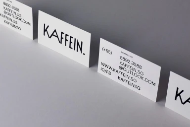 White business cards featuring black typographic branding for Kaffein displayed on a grey surface