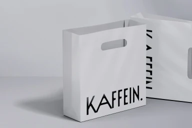 Two white paper shopping bags featuring black branding on a neutral grey and white studio background.