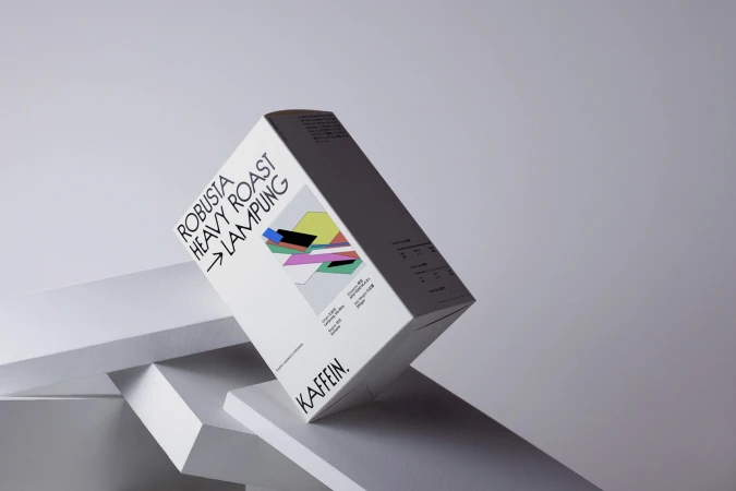 A white coffee packaging box angled on geometric white platforms against a neutral grey studio background