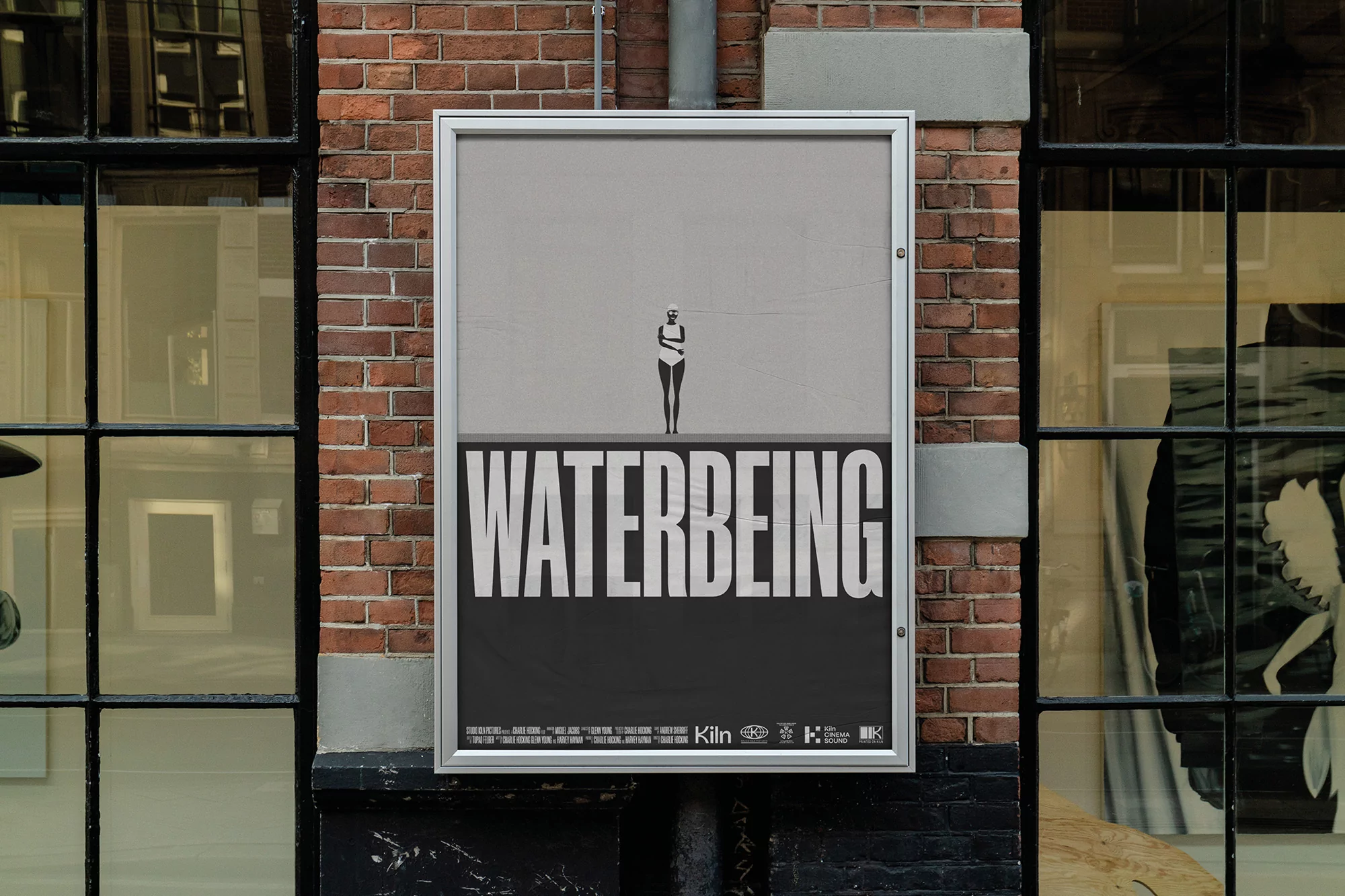 Monochromatic poster on brick wall showing woman in bathing suit standing in water, promoting 'Waterbeing' film.