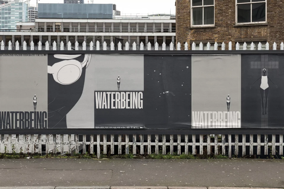 Public art installation displays five black and white panels featuring abstract swimmer figures, bold text, and urban city backdrop.