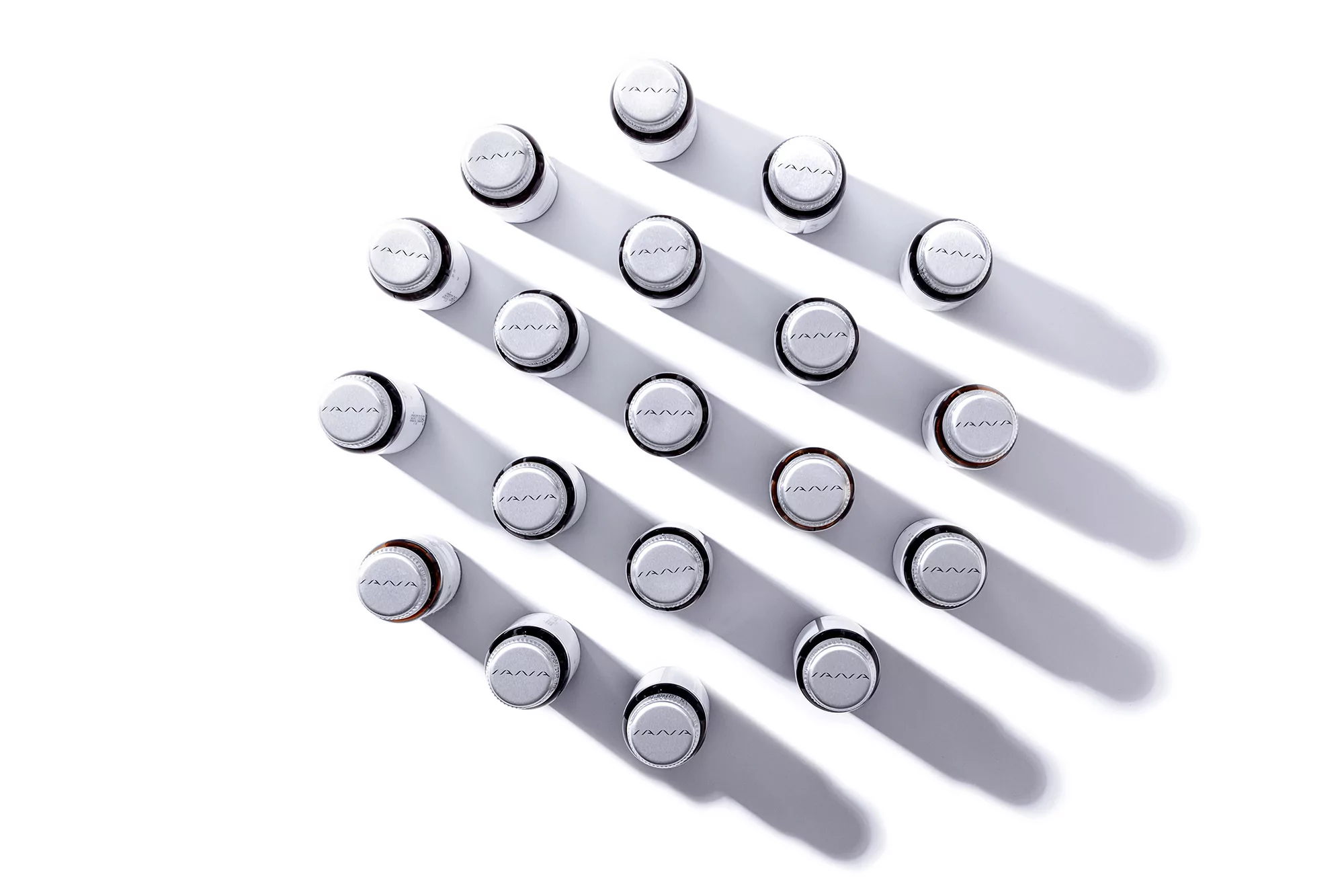Overhead shot of twenty white cosmetic bottles with black trim arranged in a grid pattern on a white surface, casting shadows.