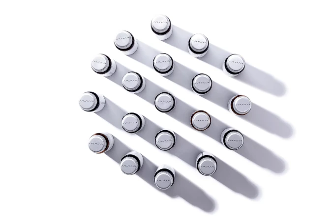 Overhead shot of twenty white cosmetic bottles with black trim arranged in a grid pattern on a white surface, casting shadows.