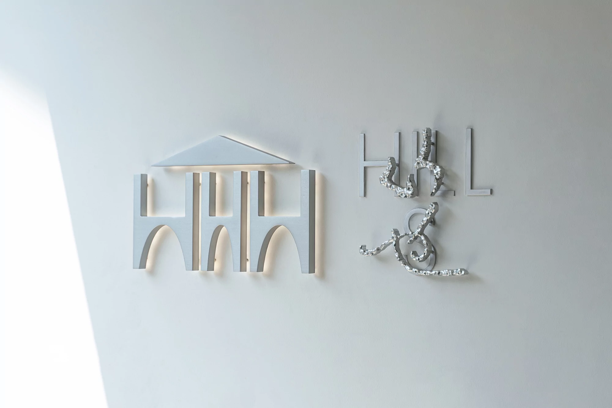 Minimalist white wall with an architectural logo featuring geometric shapes and artistic lettering for 'Hull & Hull'.