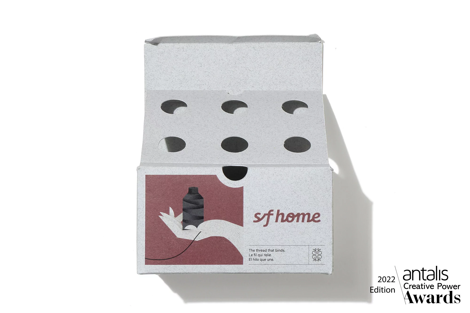 Product shot of a s/f home thread box with a spool of thread on a hand, featuring the Antalis Creative Power Awards logo.