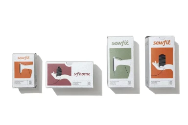 Four grey cardboard packaging boxes with colourful printed labels for Sewfil thread arranged on a white background