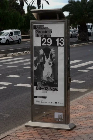 Bus stop advertisement features black and white photograph, palm trees, crosswalk, and vehicles along the side of a city street.