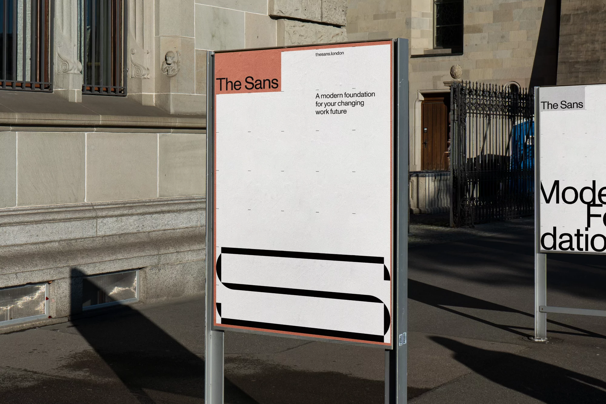 Outdoor advertisement featuring 'The Sans' typography and design, set against an urban building and street backdrop. Graphic design.