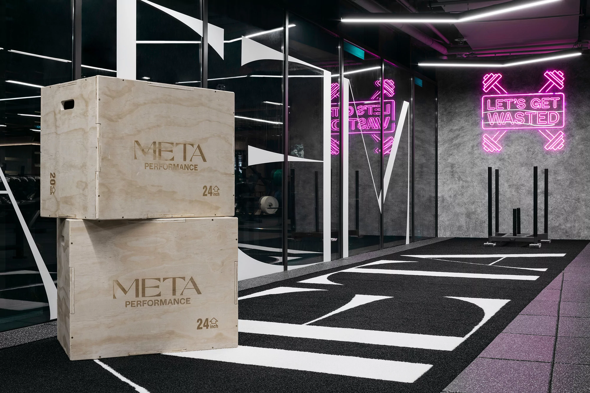 Stacked wooden plyometric boxes in a modern gym with neon signage and equipment on a black and white striped athletic track.