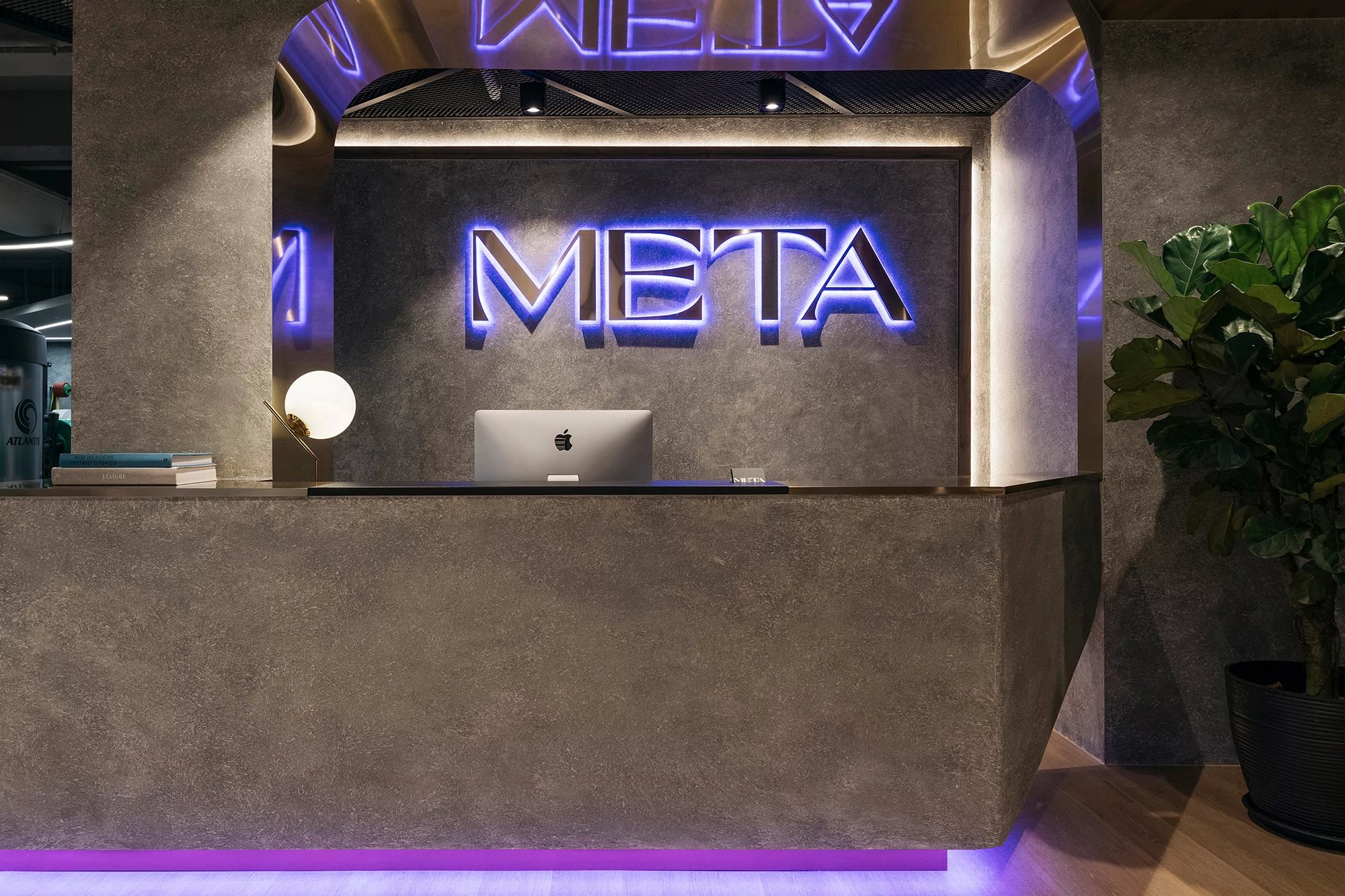 Interior of a modern office space featuring a gray reception desk with a desktop computer and a plant, lit by neon lights.