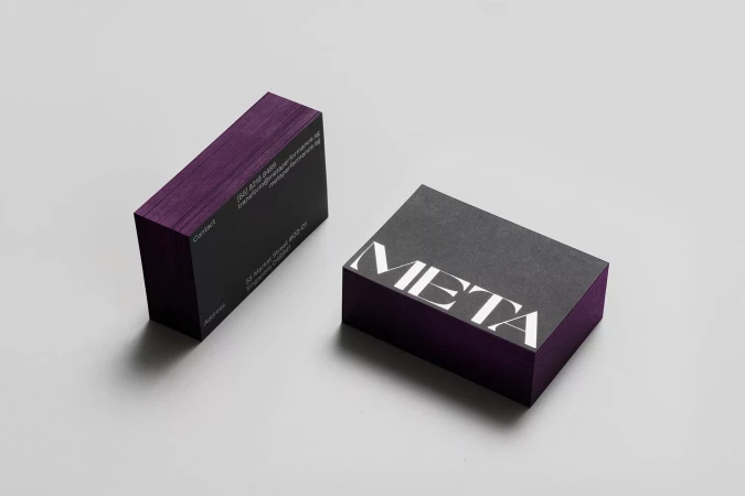 Stack of dark grey business cards with purple edges and modern, white typography on a light grey surface in a minimalist setting.