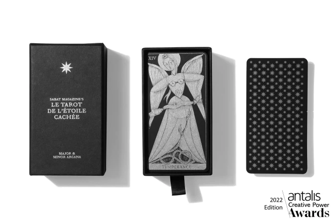 Close-up of a tarot deck featuring Sabat Magazine's 'Le Tarot de l'Étoile Cachée' with celestial artwork on a white surface. 