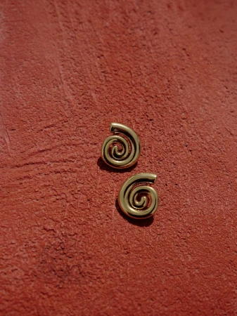 Close-up of gold spiral earrings on textured red background showcasing minimalist jewelry design and warm color palette in a studio setting.