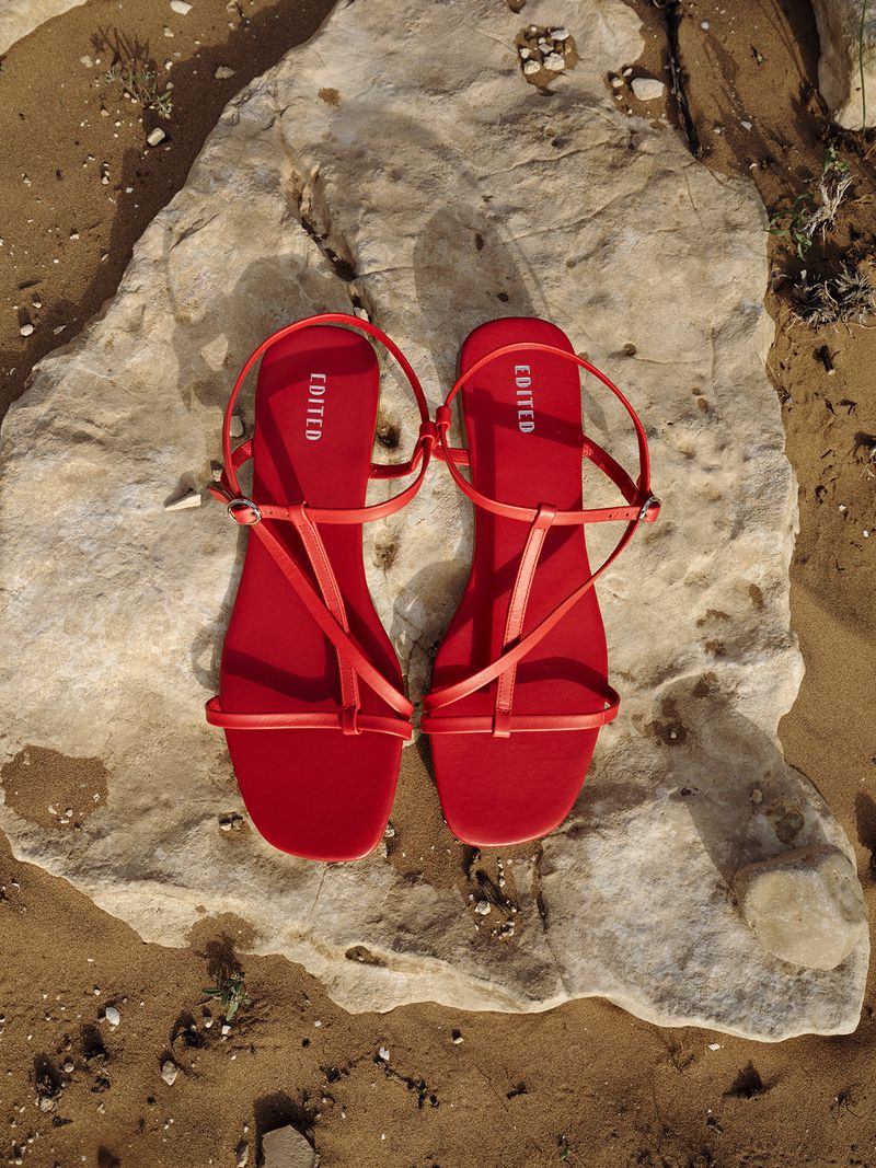 Overhead shot of two red strappy sandals placed side-by-side on a textured rock surface, with surrounding sandy ground.