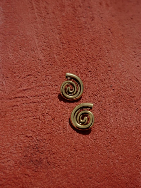 Pair of polished gold spiral earrings resting on a textured terracotta surface
