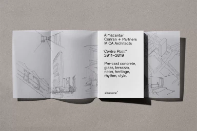 An open folded architectural brochure with hand-drawn sketches and typography displayed on a textured grey background surface.