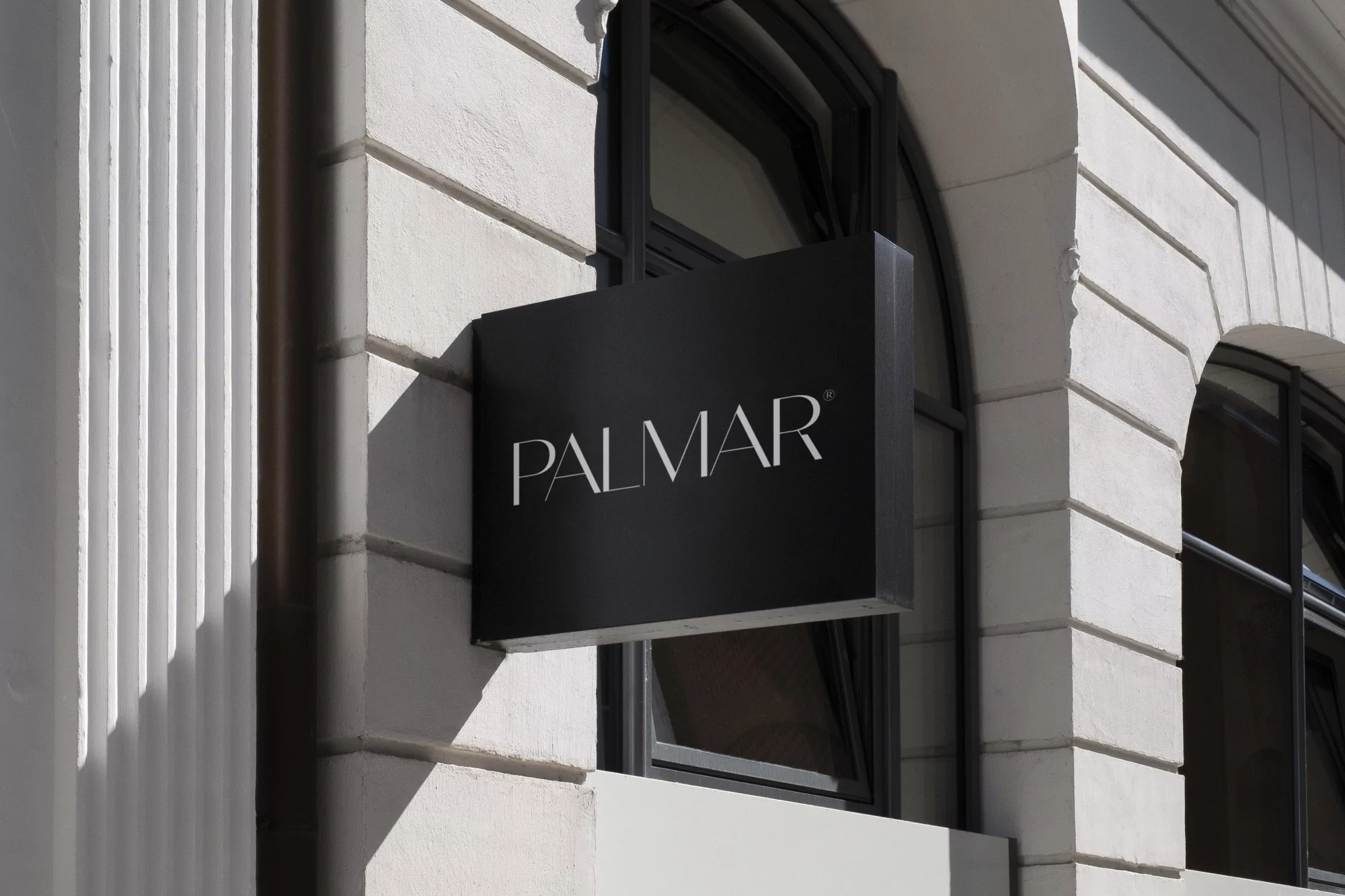 Black business signage for 'PALMAR' is mounted on a white architectural stone building with dark window frames, captured outdoors.