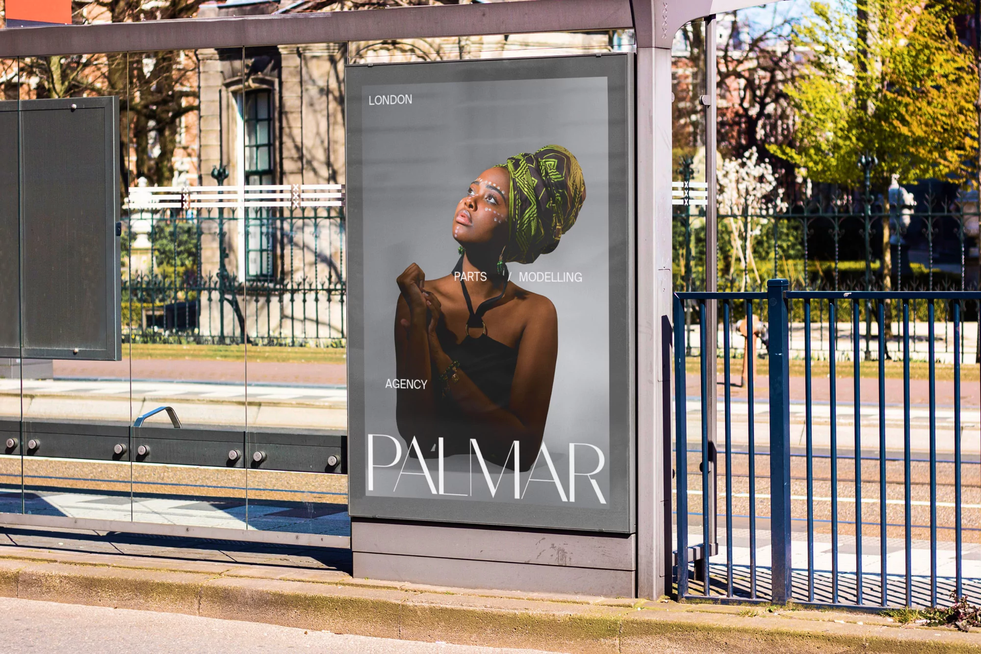 An ad in a bus stop displays a fashion shot of a Black woman wearing a patterned headwrap and jewelry, looking up against a grey backdrop.