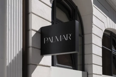 Black rectangular sign with white Palmar typography mounted on a classical white stone building exterior