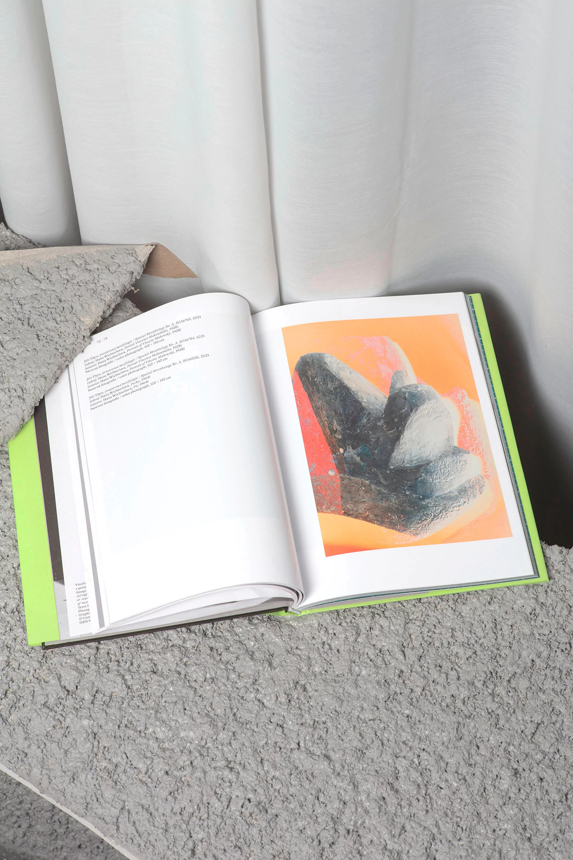 Open book on textured surface displays abstract art; bright lime green book spine stands out against neutral tones of artwork and background.