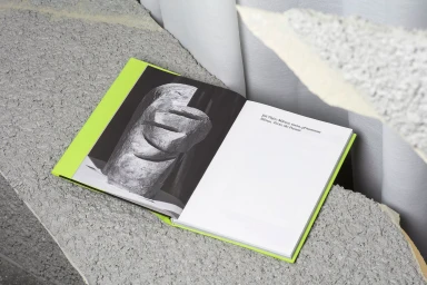 Open book with a black and white sculptural photograph on one page resting on a rough textured concrete surface.