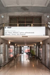 Exhibition banner for Jiri Thyn Silence Torso the Present displayed in a concrete concrete passage with stone tiled floor